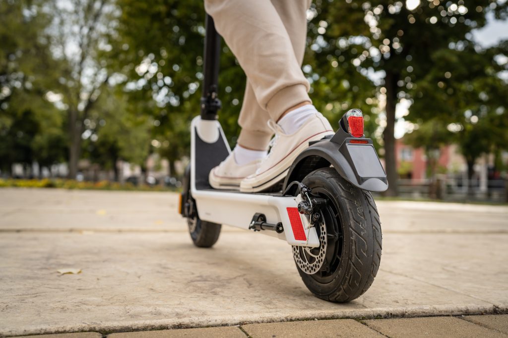 unknown man standing or driving electric kick scooter e-scooter - Guski ∙ Such - Rechtsanwälte Karlsruhe Person wearing beige pants and sneakers rides a white electric scooter; view focuses on rear wheel and brake light.